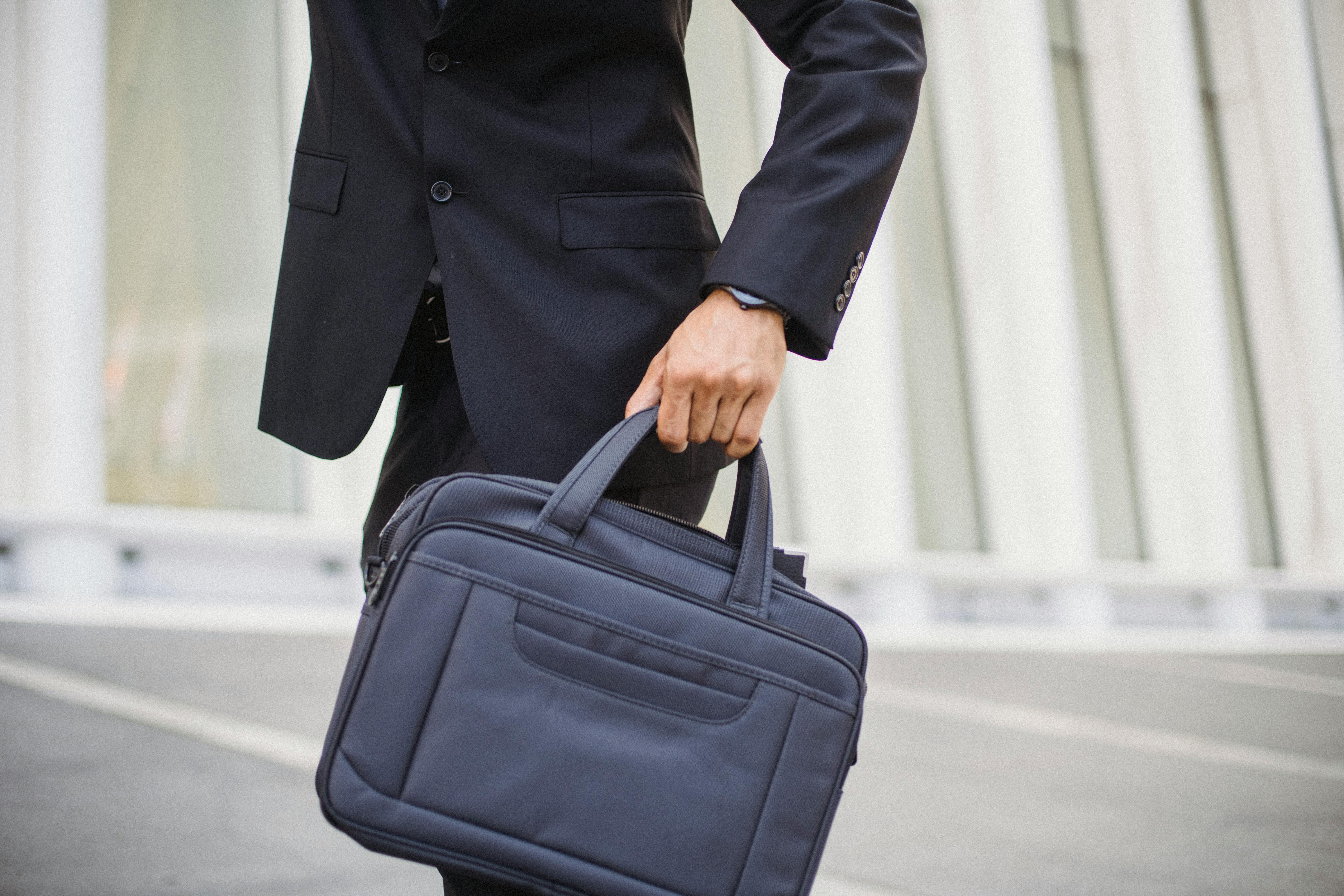 person in a black suit holding a black briefcase